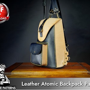 May include: A two-tone leather backpack featuring a natural tan leather top flap and back panel contrasted with dark navy blue leather side panels and a front pocket. The bag includes a buckle closure, yellow stitching, and metal hardware.