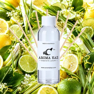Könnte beinhalten: Eine durchsichtige Glasflasche für einen Raumduft mit weißem Verschluss und einem Etikett mit der Aufschrift AROMA KAZ MADE IN AUSTRALIA, umgeben von mehreren hellen Holzstäbchen. Das Etikett zeigt ein stilisiertes C-Logo und die Website www.aromakaz.com.