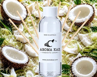 Może przedstawiać: Przezroczysta szklana butelka z białą nakrętką i etykietą z napisem AROMA KAZ EXQUISITE LUXURY MADE IN AUSTRALIA www.aromakaz.com, otoczona drewnianymi patyczkami zapachowymi, połówkami brązowych kokosów i białymi kwiatami plumerii.