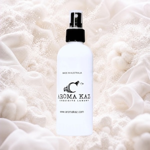 May include: A white spray bottle with a black cap, displaying the "Aroma Kaz" logo and the text "Made in Australia." The bottle is positioned against a backdrop of white fabric and powder, creating a clean and luxurious aesthetic.