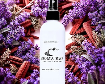 May include: A white spray bottle with a black cap, featuring the text "AROMA KAZ EXQUISITE LUXURY" and "Made in Australia." The bottle is surrounded by purple lavender flowers and reddish-brown wood chips, creating a natural aesthetic.