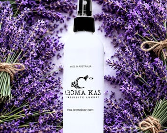 May include: White spray bottle with a black cap, featuring the text "AROMA KAZ EXQUISITE LUXURY" and "Made in Australia." The bottle is surrounded by bundles of purple lavender flowers, tied with twine.