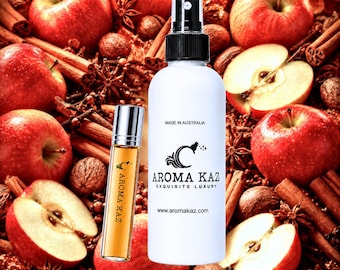 May include: A white spray bottle and a small glass roller bottle filled with amber liquid, both labeled AROMA KAZ. The spray bottle features the text MADE IN AUSTRALIA and www.aromakaz.com. The background is filled with red apples, cinnamon sticks, and star anise.