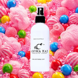 Può includere: Un flacone spray bianco con tappo nero e la scritta "AROMA KAZ EXQUISITE LUXURY" è centrato davanti a uno sfondo di caramelle colorate. La bottiglia riporta anche la scritta "MADE IN AUSTRALIA" e "www.aromakaz.com".