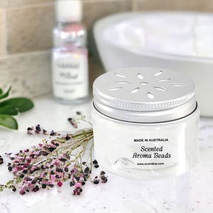 Handmade scented aroma beads air freshener jar in bathroom setting beside sink and flowers, made in Australia, long-lasting vegan and cruelty-free home fragrance for bathrooms, wardrobes and small spaces.