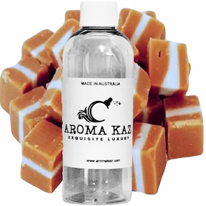 May include: A clear glass bottle with a white cap and a white label. The label has black text that reads "Aroma Kaz Exquisite Luxury" and "www.aromakaz.com". The bottle is surrounded by a pile of caramel sweets with white stripes.