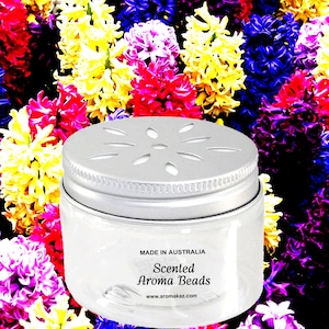 May include: A clear jar with a silver lid, containing scented aroma beads. The lid has decorative cutouts. The text "MADE IN AUSTRALIA" and "Scented Aroma Beads" are printed on the jar. The background is a colorful array of flowers.