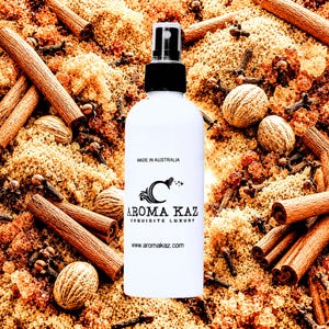 May include: White spray bottle with a black cap, featuring the "Aroma Kaz" logo and text. The bottle is surrounded by cinnamon sticks, nutmeg, and brown sugar. The text "Made in Australia" and the website address are also visible.