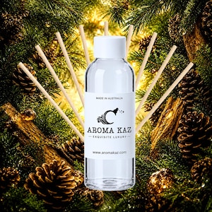 Op de afbeelding: Een doorzichtige glazen fles voor een geurverspreider met een witte dop en een wit etiket met de tekst MADE IN AUSTRALIA, AROMA KAZ, EXQUISITE LUXURY en www.aromakaz.com, omringd door verschillende dunne houten rietjes in een waaier.