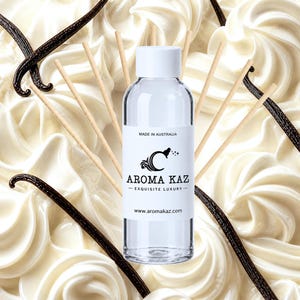 May include: A clear cylindrical bottle with a white cap and a label reading AROMA KAZ EXQUISITE LUXURY MADE IN AUSTRALIA www.aromakaz.com, surrounded by several thin wooden reeds, positioned against a background of white cream swirls and vanilla beans.