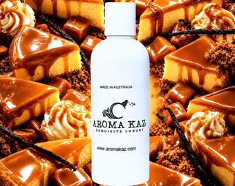May include: A white cylindrical bottle with a cap, featuring the text MADE IN AUSTRALIA, the AROMA KAZ logo, EXQUISITE LUXURY, and www.aromakaz.com, centered over a background of caramel-drizzled cheesecake slices, whipped cream, and vanilla beans.