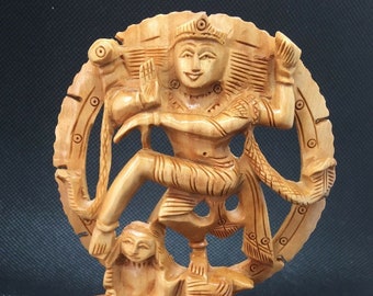 May include: A wooden sculpture of the Hindu god Shiva in his Nataraja form, dancing on a demon. The sculpture is carved in a light brown color and features intricate details. The sculpture is standing on a base with a decorative design.