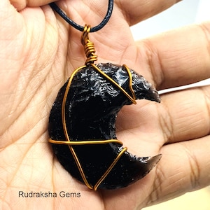 Könnte beinhalten: Ein schwarzer Obsidian-Halbmond-Anhänger, der mit goldfarbenem Draht umwickelt ist und an einer schwarzen Schnurkette hängt. Rudraksha Gems.