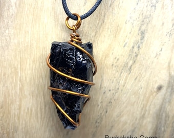 May include: Black obsidian pendant wrapped in copper wire, hanging from a black cord necklace. The pendant is a rough, natural shape and has a glossy finish.  Rudraksha Gems is printed below the pendant.