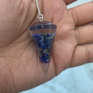 May include: A clear crystal pendulum with a silver chain. The pendulum is filled with blue and gold flecks.