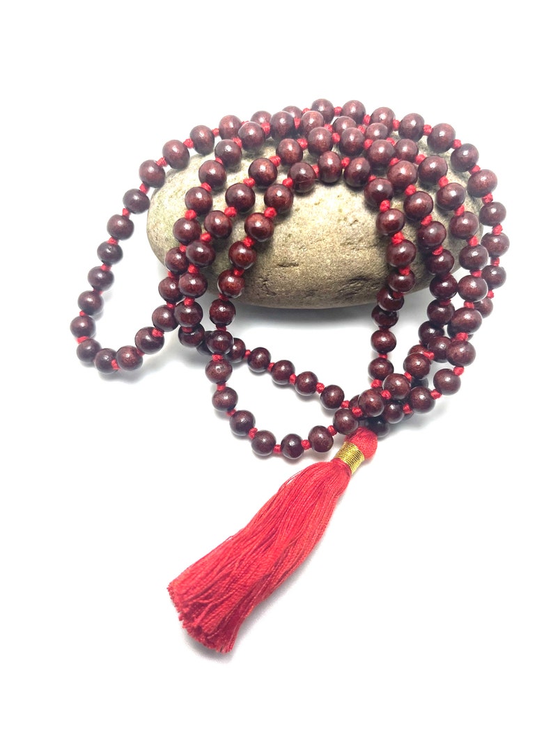 May include: A red wooden mala bead necklace with a red tassel. The beads are strung on a red cord and the tassel is attached to the end of the cord.