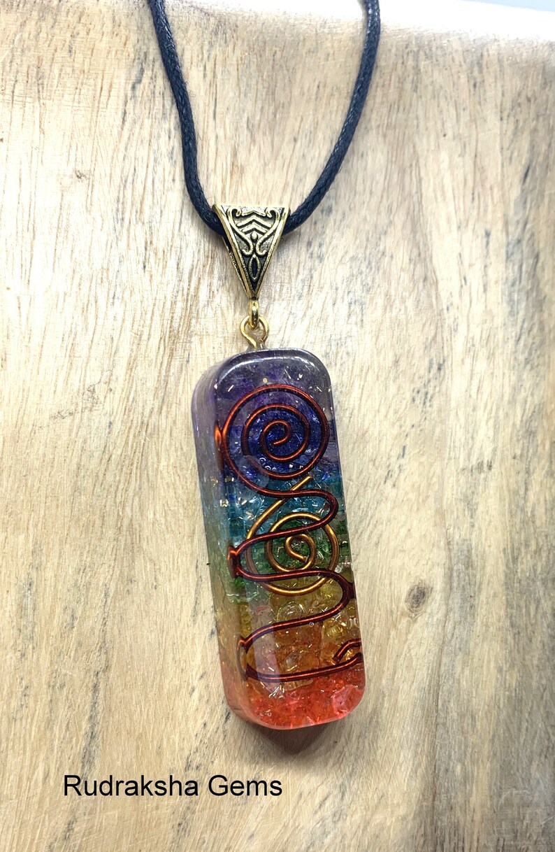 May include: A rainbow colored seven chakra crystal pendant with a gold wire spiral design. The pendant is on a black cord.