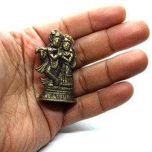 Puede incluir: Una peque&ntilde;a estatua de metal dorado de una pareja de pie juntos. La figura masculina sostiene una flauta y la figura femenina sostiene una flor. La estatua est&aacute; sobre una peque&ntilde;a base redonda.