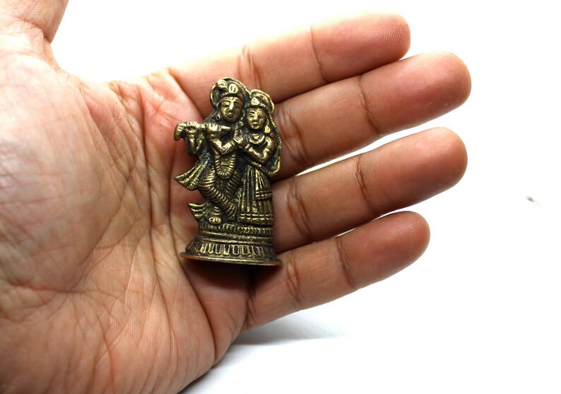 Puede incluir: Una peque&ntilde;a estatua de metal dorado de una pareja de pie juntos. La figura masculina sostiene una flauta y la figura femenina sostiene una flor. La estatua est&aacute; sobre una peque&ntilde;a base redonda.