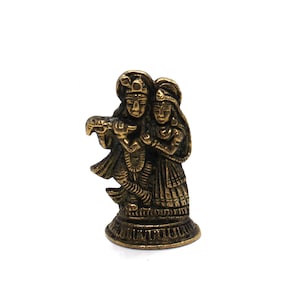 Puede incluir: Una peque&ntilde;a estatua de metal de color dorado de una pareja de pie juntos. La figura masculina sostiene una flauta y la figura femenina sostiene una flor. La estatua est&aacute; sobre un fondo blanco.