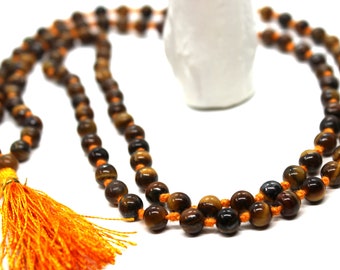 May include: A brown and gold tiger's eye mala bead necklace with an orange tassel. The necklace is made of 108 beads and is strung on a thin orange cord.