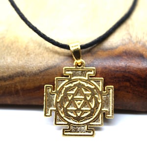 Op de afbeelding: Gouden ketting met hanger in geometrisch ontwerp, met een centrale cirkel met een ster erin. De hanger is aan een zwart koord.