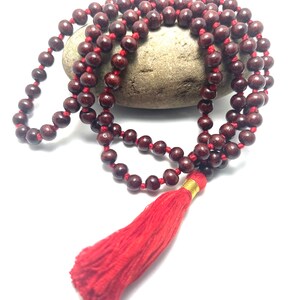 May include: A red wooden mala bead necklace with a red tassel. The beads are strung on a red cord and the tassel is attached to the end of the cord.