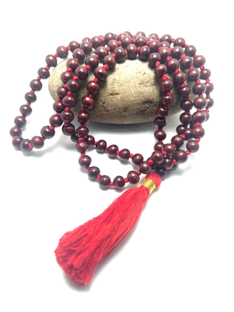 May include: A red wooden mala bead necklace with a red tassel. The beads are strung on a red cord and the tassel is attached to the end of the cord.