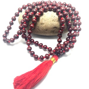 May include: A red wooden mala bead necklace with a red tassel. The beads are strung on a red cord and the tassel is attached to the end of the cord.