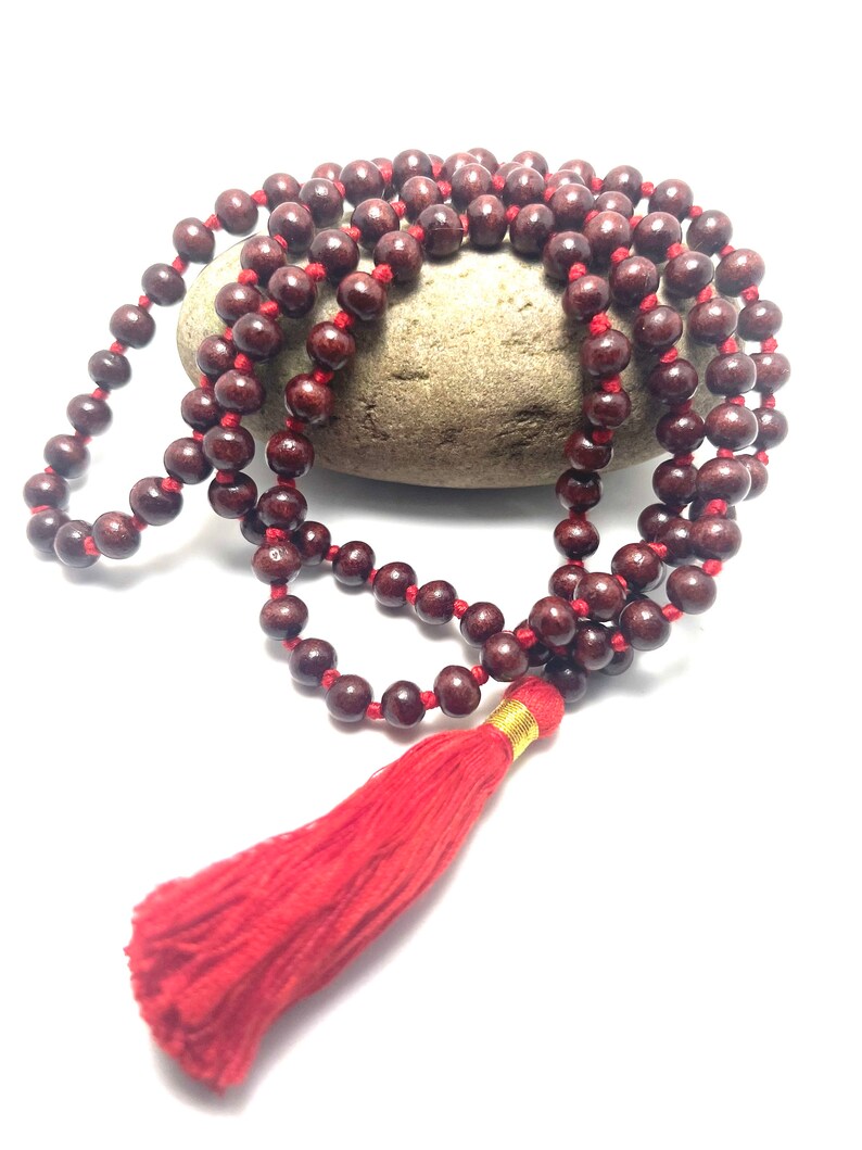 May include: A red wooden mala bead necklace with a red tassel. The beads are strung on a red cord and the tassel is attached to the end of the cord.