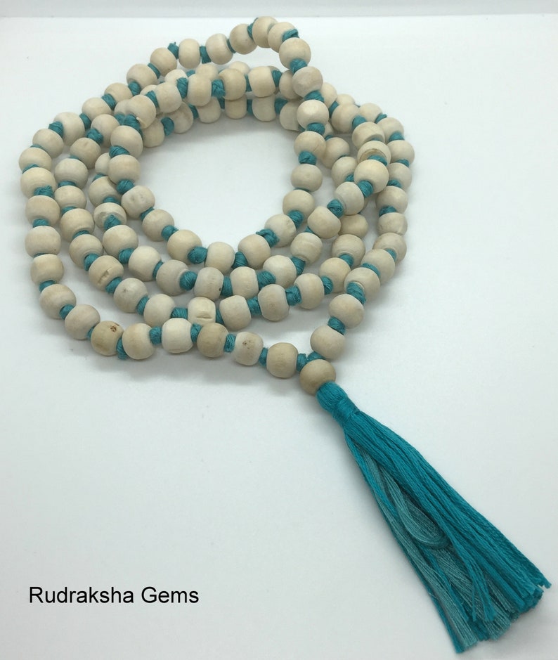 May include: A long strand of light beige wooden beads strung on a vibrant turquoise cord, arranged in a circular pattern. The necklace features a matching turquoise tassel at the bottom and includes the text Rudraksha Gems in the corner.