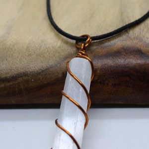 May include: A white selenite crystal wrapped in copper wire, hanging from a black cord necklace.