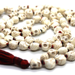 May include: A necklace with off-white skull-shaped beads and red accents. It has a dark red and black tassel. The beads are strung together, forming a distinctive and edgy accessory. The necklace is a unique piece of jewellery.