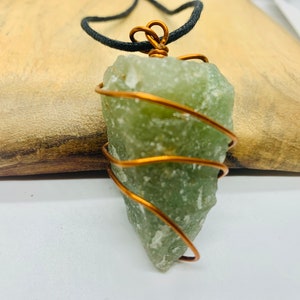 May include: A green crystal pendant wrapped in copper wire, hanging from a black cord.