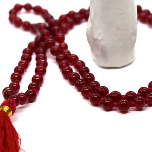 Puede incluir: Un collar mala de cuentas rojas con un borla. Las cuentas son redondas y tienen un acabado brillante. La borla está hecha de hilo rojo y tiene un acento dorado.