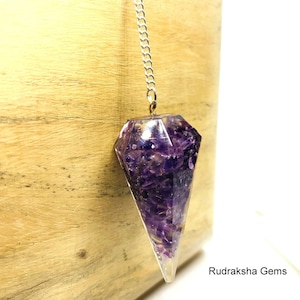 Könnte beinhalten: Ein violetter Amethyst-Kristall-Pendel mit einer silbernen Kette. Der Kristall ist in klarem Harz eingeschlossen und hat eine facettierte Form.