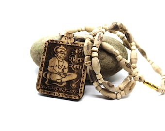 May include: A rectangular wooden pendant featuring an engraved image of a seated deity and Devanagari script, suspended from a necklace made of light-colored, textured wooden beads with a small gold-toned cylindrical clasp connector.