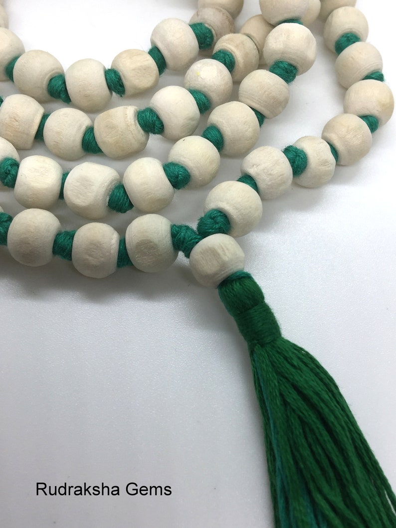 May include: A string of light-coloured, round wooden beads separated by knots on a vibrant green cord. The strand features a prominent green tassel at one end. The text "Rudraksha Gems" is printed in the bottom left corner of the image.
