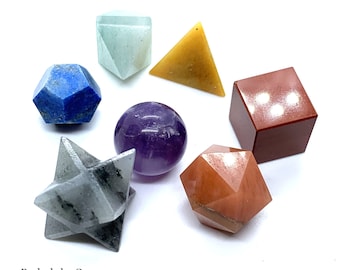 Puede incluir: Conjunto de siete cristales de forma geométrica en varios colores, incluyendo azul, verde, morado, naranja y rojo. Los cristales están dispuestos sobre una superficie blanca. Rudraksha Gems está escrito en texto negro en la parte inferior de la imagen.
