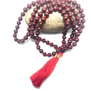 May include: A red wooden mala bead necklace with a red tassel. The beads are strung on a red cord and the tassel is attached to the end of the cord.