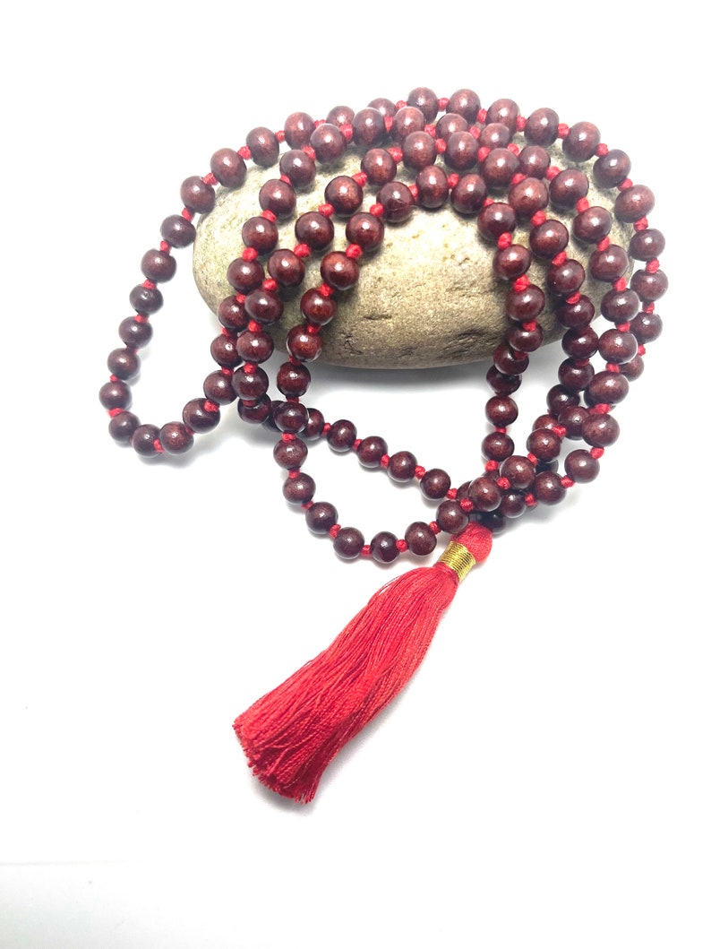 May include: A red wooden mala bead necklace with a red tassel. The beads are strung on a red cord and the tassel is attached to the end of the cord.