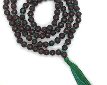May include: A brown wooden mala bead necklace with a green tassel. The beads are strung on a green cord. The necklace is called "Rudraksha Gems".