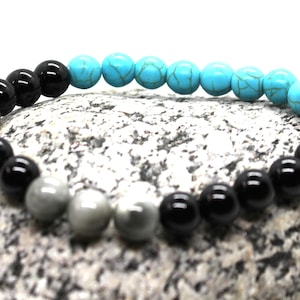 May include: A beaded bracelet with black, gray, and turquoise beads. The bracelet is on a gray rock.