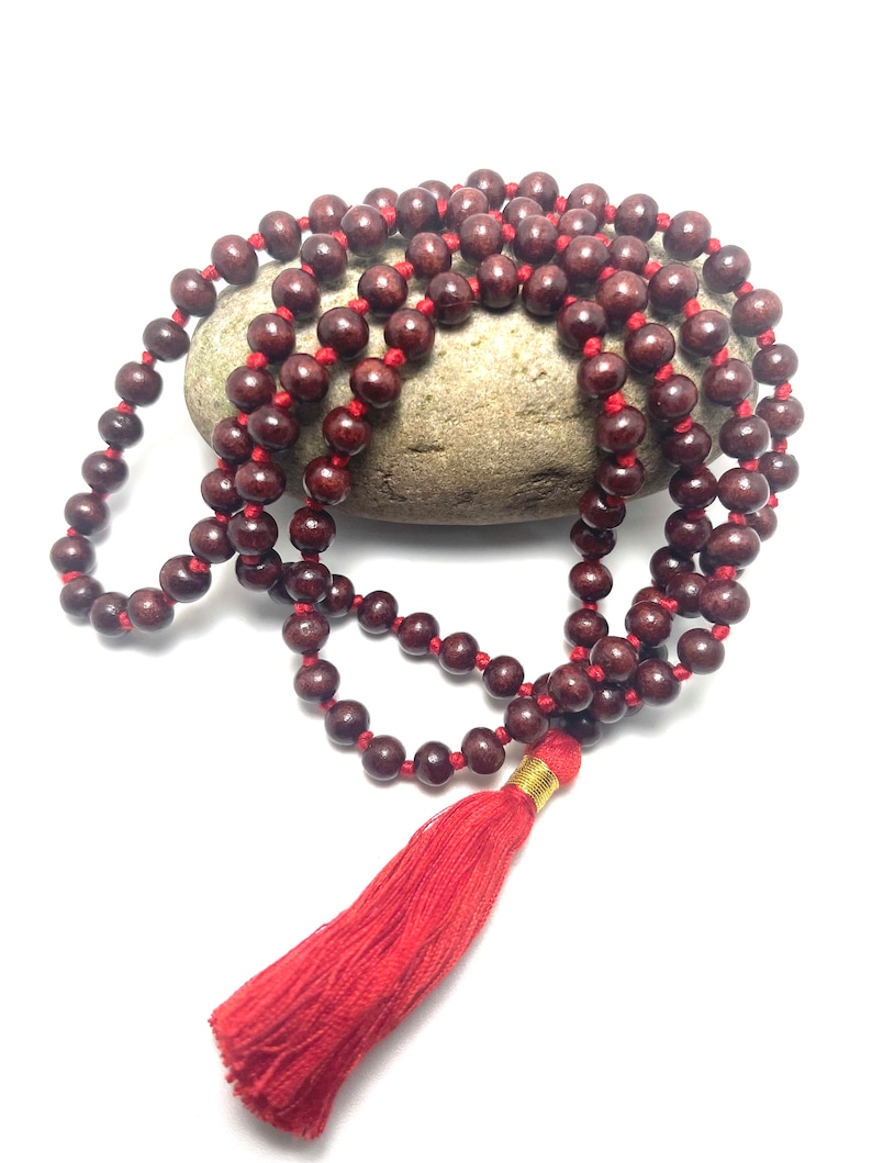 May include: A red wooden mala bead necklace with a red tassel. The beads are strung on a red cord and the tassel is attached to a gold bead.