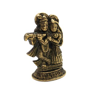 Puede incluir: Una estatua de metal dorado de una pareja, probablemente representando a Krishna y Radha, de pie uno junto al otro. La figura masculina sostiene una flauta en su mano.