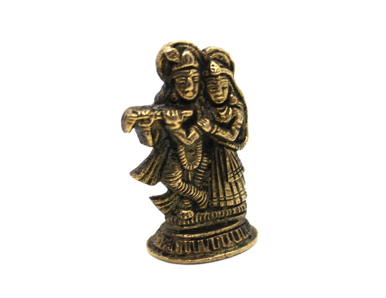 Puede incluir: Una estatua de metal dorado de una pareja, probablemente representando a Krishna y Radha, de pie uno junto al otro. La figura masculina sostiene una flauta en su mano.