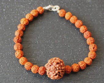 May include: A bracelet composed of small, round, textured brown rudraksha beads strung together, featuring one significantly larger, central rudraksha bead and a silver-toned metal lobster claw clasp closure at the top.