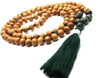 May include: A wooden mala bead necklace with a green tassel. The beads are brown and the tassel is made of a dark green fabric.