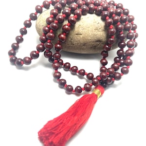 May include: A red wooden mala bead necklace with a red tassel. The beads are strung on a red cord and the tassel is attached to the end of the cord.