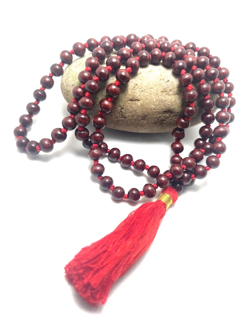 May include: A red wooden mala bead necklace with a red tassel. The beads are strung on a red cord and the tassel is attached to the end of the cord.